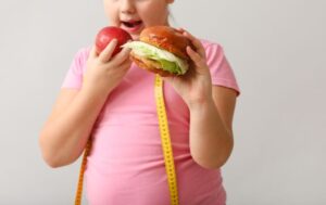 Overweight girl with healthy and unhealthy food on light background